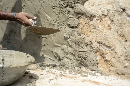 close up image of textured surface with mortar mixture-cropped hand with a working tool outside- building concept