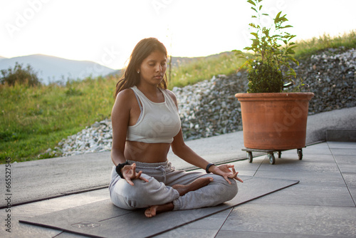 Girl practices outdoor yoga meditation in nature. On the horizon the sunset with its light illuminating her face. 