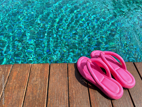 Clear rippled water in swimming pool and pink flip-flops on wooden deck outdoors. Space for text