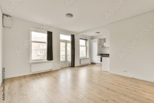 an empty living room with hardwood flooring and white walls  large windows in the room is light wood floors