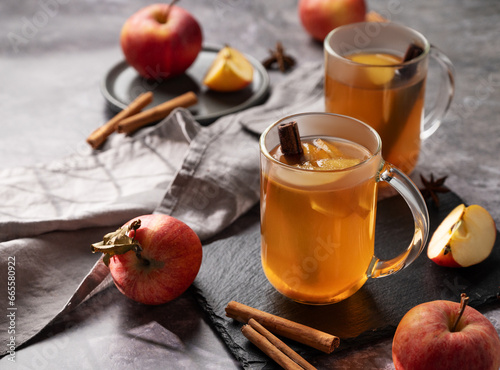 Homemade apple punch with fresh apples, cinnamon and spices in cups on dark background with fresh fruits. A hot, healthy autumn or winter drink.