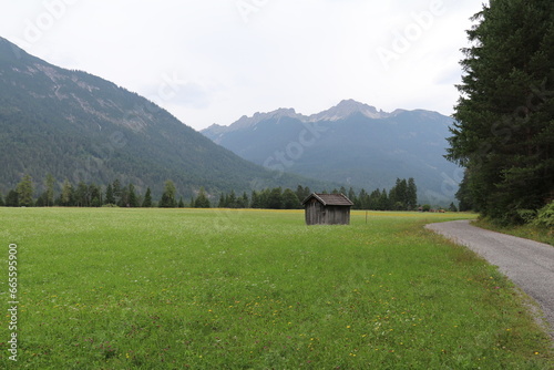 little wooden mountain shed in a pastural meadow surrounded by mountains