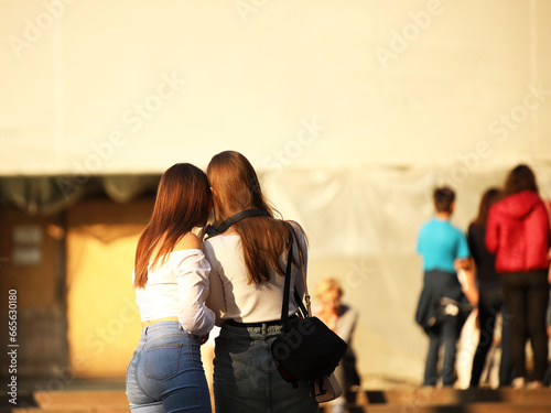 Young long-haired brown-haired girls walk in the center of the ancient city. Fashion of modern youth. Free time and happy weekend. Blurred background. Ancient architecture and design of buildings