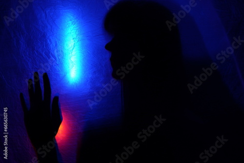 Arms of woman pressing against curtain. silhouette woman behind blue light poses mysteriously and artistically