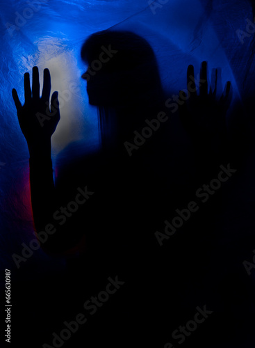 silhouette woman behind blue light poses mysteriously and artistically