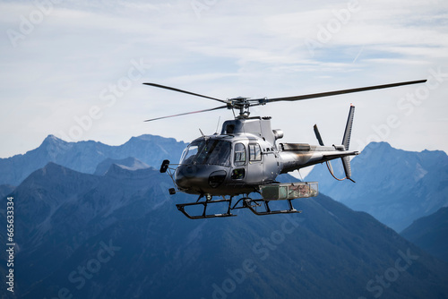 Fototapeta Naklejka Na Ścianę i Meble -  Dark gray cargo helicopter with accessories basket on the side flies in the mountains of the Tyrolean Alps