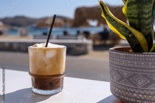 View of an iced Greek  coffee, also known as freddo cappuccino with a straw and the beach of Gialos in Ios Greece photo