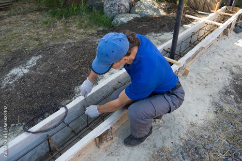 A worker knits rebar for pouring the foundation of the fence.