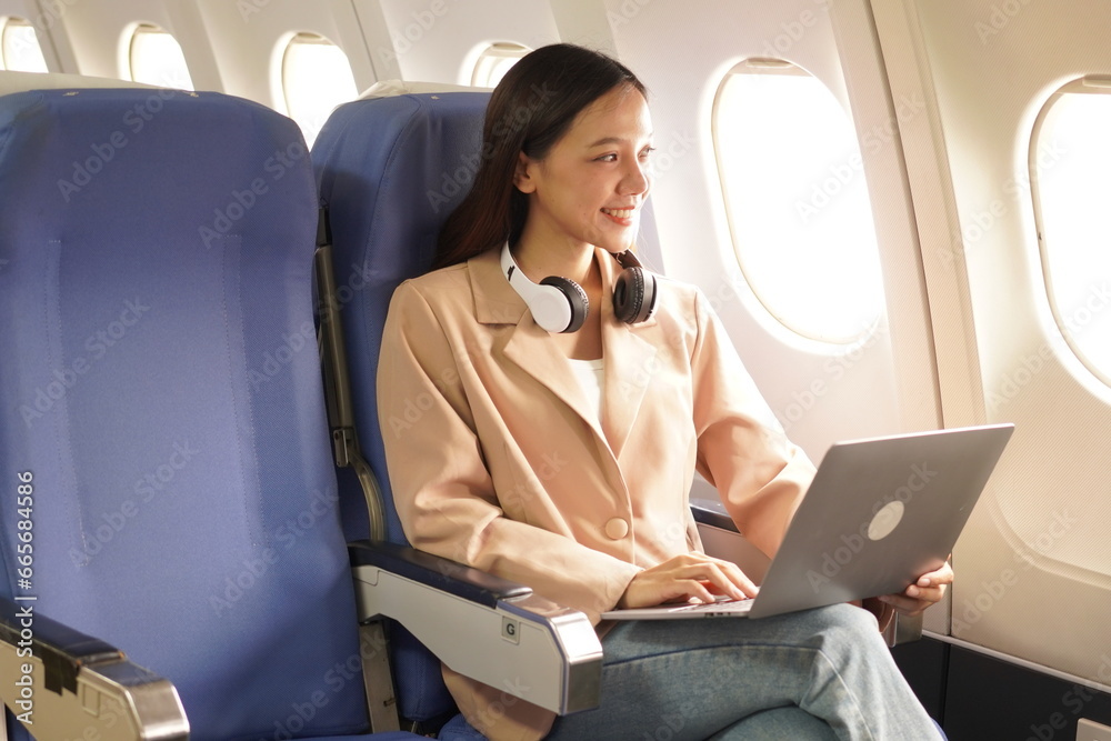 Asian woman sitting on airplane playing with cell phone and looking out window on vacation travel concept Talk about business on airplanes, listen to music, watch movies, relax, travel.