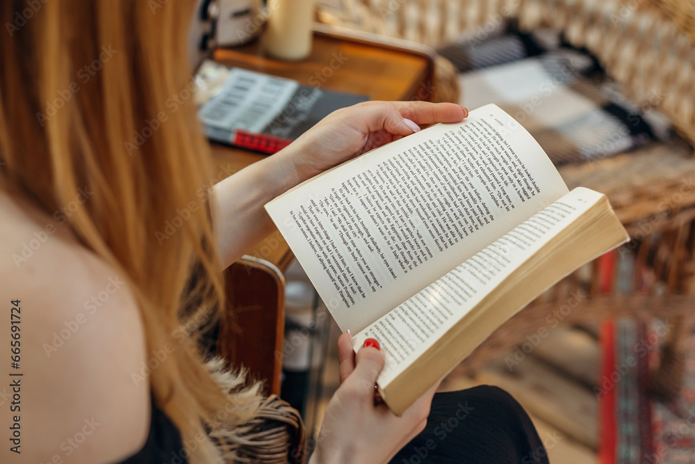 Obraz premium female hands holding a vintage book. girl reading a book sitting on a straw chair
