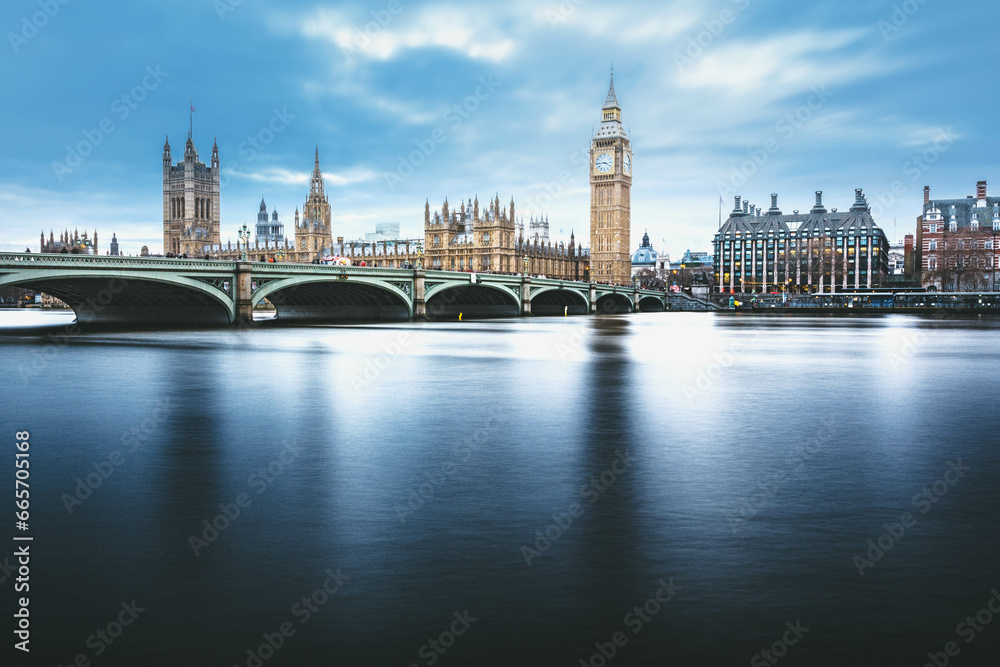 Naklejka premium Daytime London skyline featuring Westminster Bridge, the Big Ben, and other iconic landmarks against a backdrop of blue sky. Explore the beauty of Westminster in London.