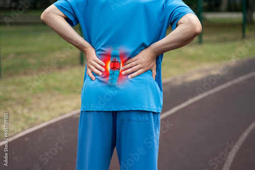 Lumbar intervertebral spine hernia, man with back pain on a running track after workout, spinal disc disease