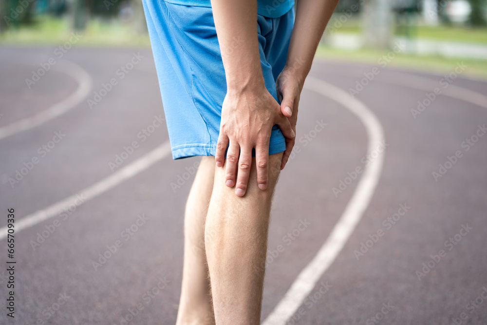 Diseases of the knee joint, bone fracture and inflammation, athletic man on a running track after workout suffering from pain in leg and doing self-massage