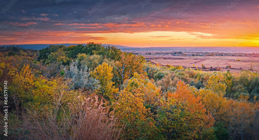 Colorful autumnal landscape. Beautiful view over the valley to the forest sunlit by the warm sunset light. Picturesque fall season scenery