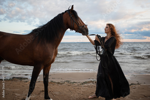 beautiful young rider in a dress and with her hair down, leads her horse along the beach. horseback riding in the open air