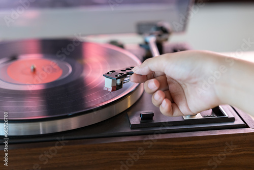 Close up woman hand put the needle on a record, playing vinyl disc at the party. Female dropping the needle on a long playing vinyl record. Music on vinyl discs. photo