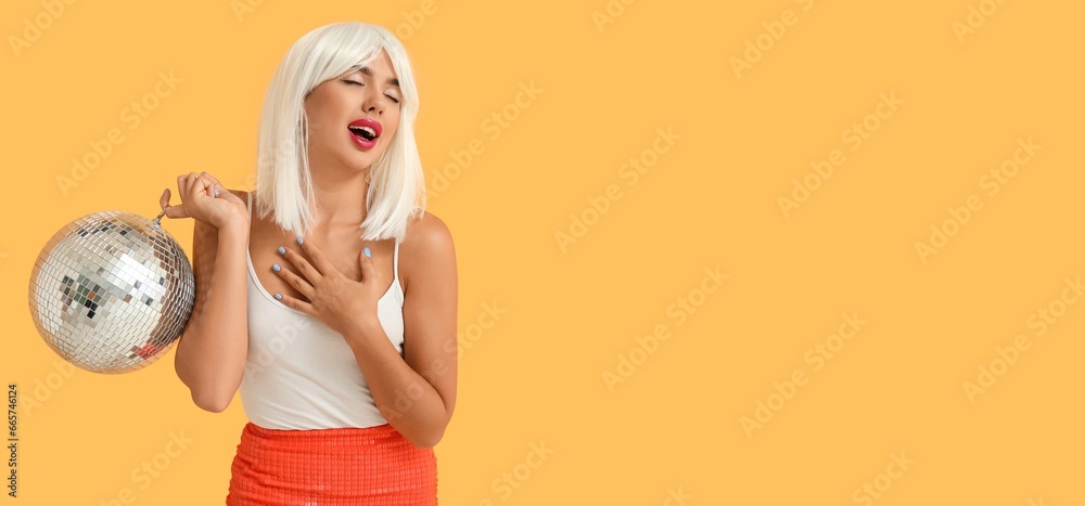 Portrait of beautiful young woman in wig and with disco ball on yellow background with space for text Portrait of beautiful young woman in wig and with disco ball on yellow background with space for text