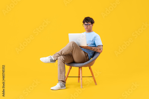 Male programmer with laptop sitting in chair on yellow background