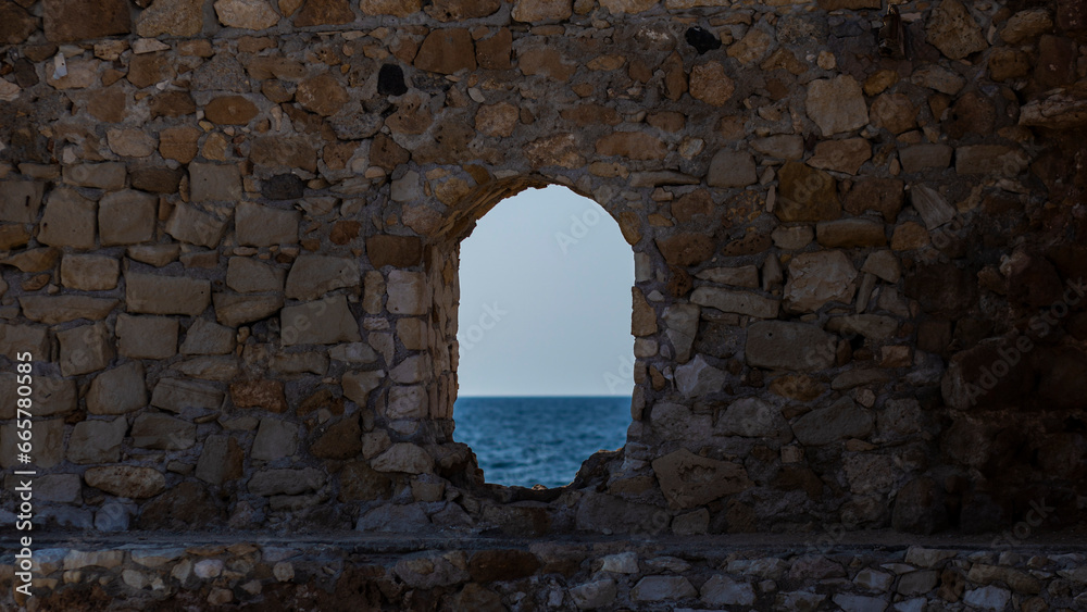 Rock wall with a window hole to the blue quiet Mediterranean Sea, in Chania, Crete, Greek Islands