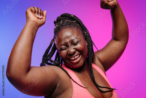 Joyful African plus size woman in sportswear gesturing and smiling on vibrant background