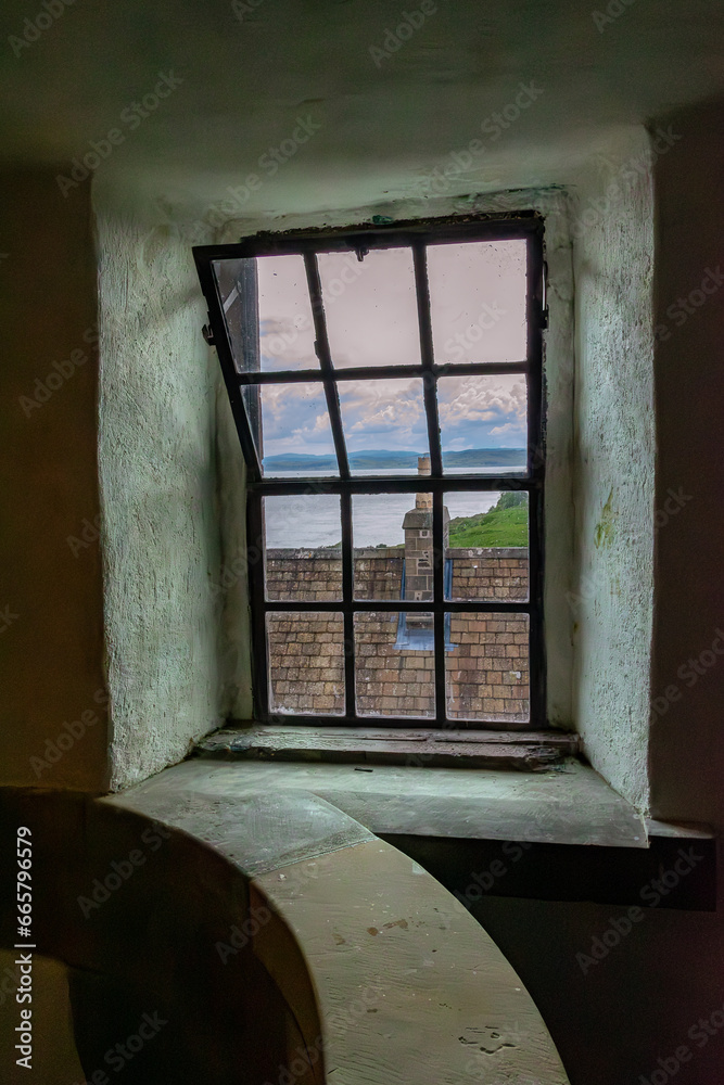 Looking through an ancient castle stairwell window at the pink sky sunset over the Loch. Duart Castle, Scotland