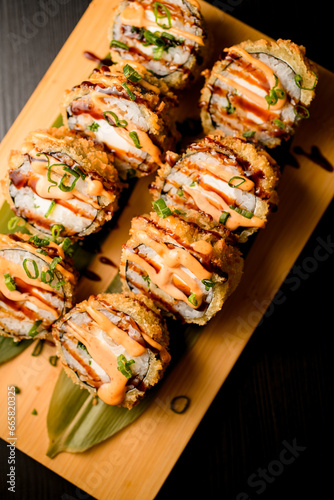 Baked sushi rolls with salmon, cheese and sauce on a wooden board close up