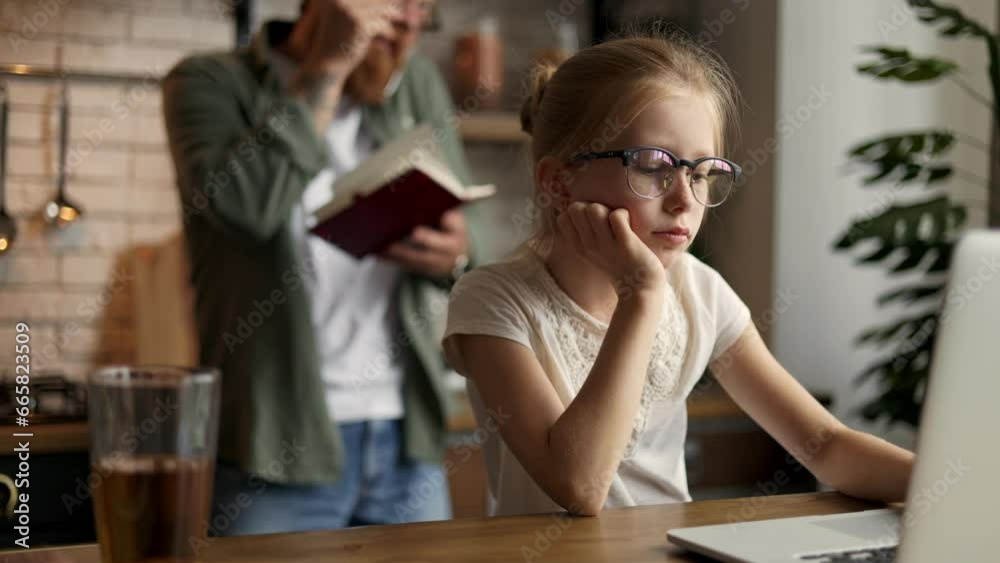 Sad kid using laptop near blurred busy father talking on smartphone at home Sad kid using laptop near blurred busy father talking on smartphone at home
