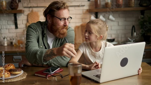 Child using laptop with tattooed father and talking near buns in kitchen at home photo