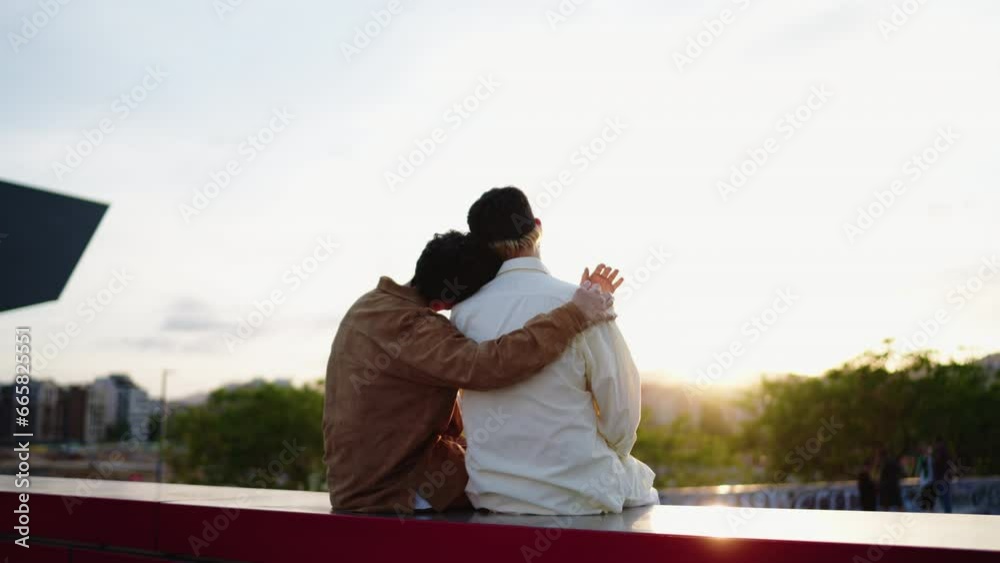Romantic male LGBT couple in love admiring beautiful sunset while sitting outdoors.Affectionate warm embrace, depth of gay affection while enjoying their unique homosexual journey together during date