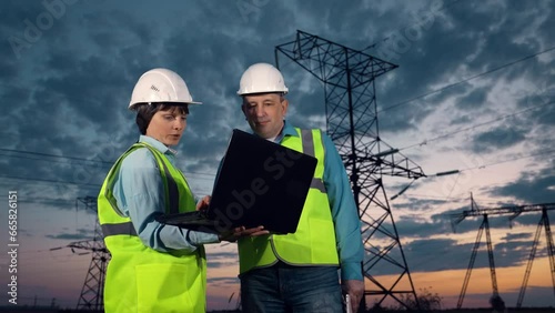 Engineer shows project on laptop to taskmaster by power transmission lines photo