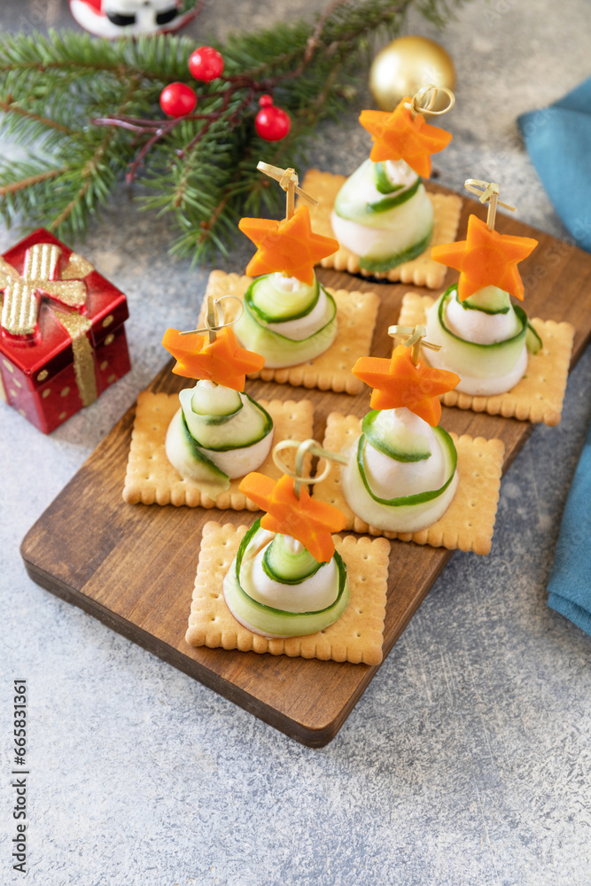 Creative appetizers christmas. Christmas trees of ham, cucumber, cheese and star of carrot on crackers on the festive table. Copy space.