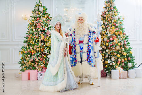 a Father Frost and Snow Maiden in blue costume in the room with christmas trees 