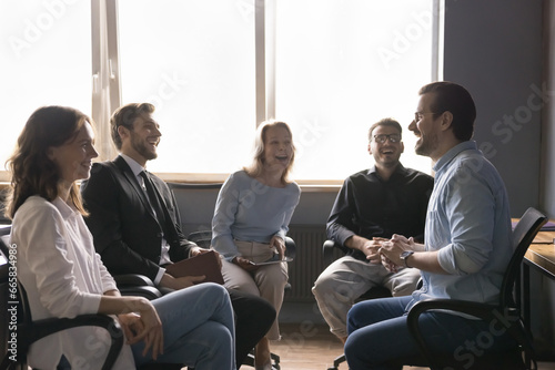 Positive smiling team of diverse professional sit in chairs in circle laugh on corporate briefing, discuss successful project. Man leader met with employees in modern office have fun talking, laughing