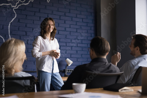 Smiling woman business speaker talk to audience of company employees, conducts corporate seminar for advanced training. Group of positive people gather together to solve work tasks. Teamwork, briefing