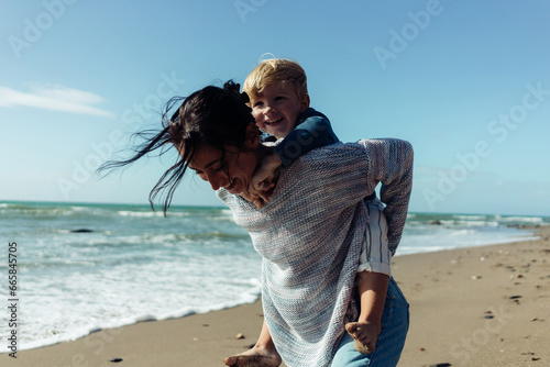 Fotografi A happy mother holds her smiling son in her arms by the sea, enjoying the view