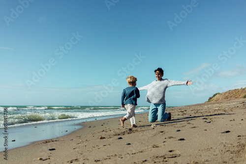 A young mother and her three-year-old son run, play, smile, and laugh on the seashore.