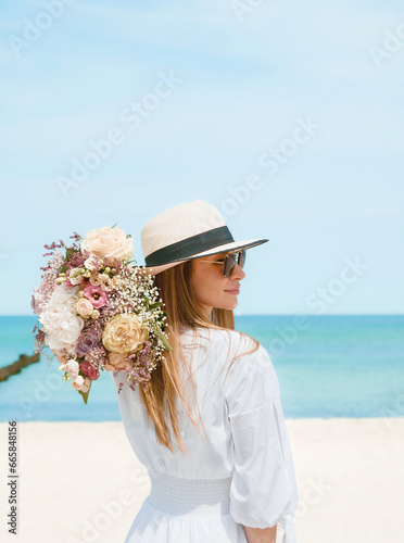 Obraz na płótnie Joyful Young Woman Holding a Bouquet of Flowers on a Beach with Blue Sky Background w salonie