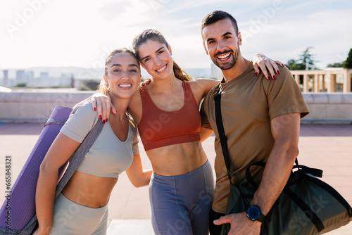 Young group of sportive friends smiling at camera standing together outdoor after workout routine. Fitness people and personal trainer occupation concept.