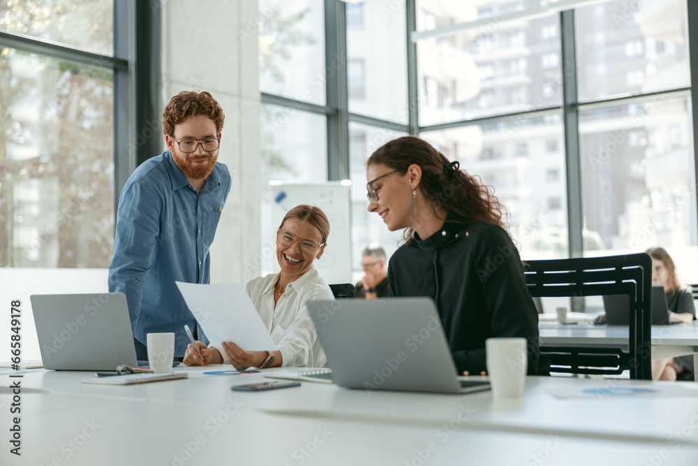 Group of young business people discussing something and smiling while sitting at the office table Group of young business people discussing something and smiling while sitting at the office table
