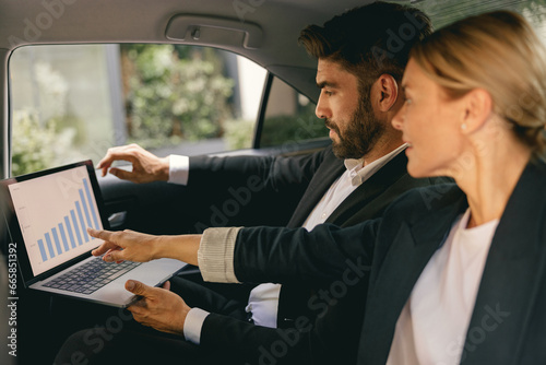 Business colleagues working on laptop in back seat of car while traveling to meeting © Yaroslav Astakhov