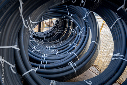 Coils of black polyethylene pipes for laying high voltage electrical cables underground at a construction site. Electrical insulation