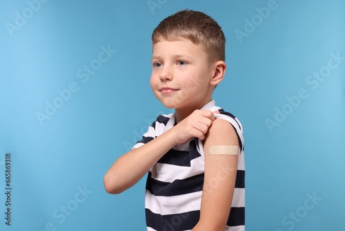 Boy with sticking plaster on arm after vaccination against light blue background