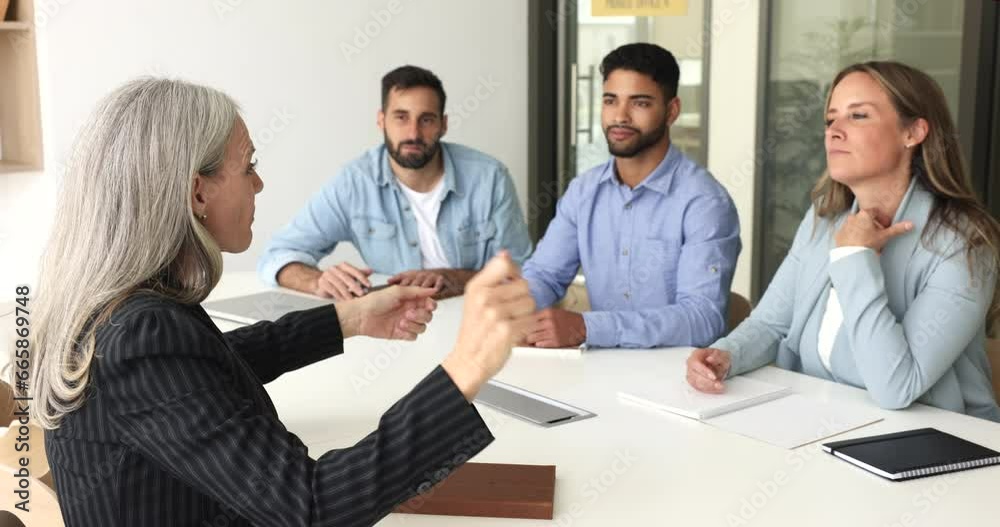 Mature female boss talk to employees during meeting in boardroom, sit at table, speaking, instructing business team, explaining project details, motivating for successful teamwork. Training, mentoring Mature female boss talk to employees during meeting in boardroom, sit at table, speaking, instructing business team, explaining project details, motivating for successful teamwork. Training, mentoring