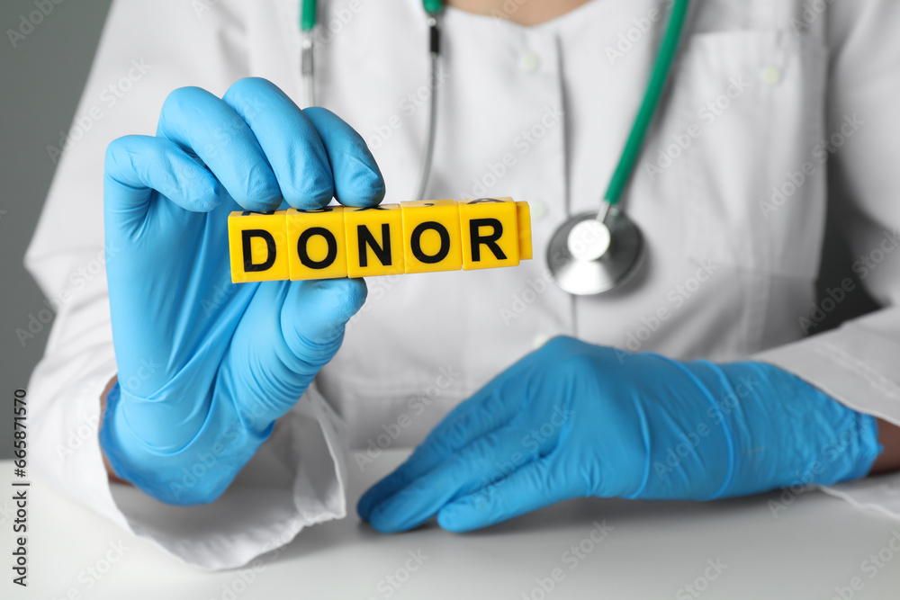 Doctor holding word Donor made of cubes at white table, closeup