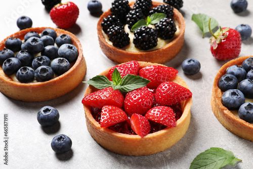 Tartlets with different fresh berries on light grey table. Delicious dessert