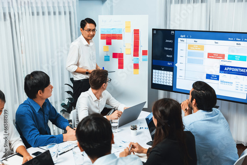 Project manager communicate and collaborate with team using project management software display on monitor  tracking progress of project task and making schedule plan at meeting table. Prudent