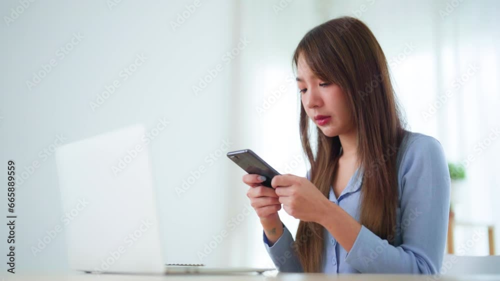 Young asian woman talking mobile smartphone while working on computer laptop on desk in living room at home Young asian woman talking mobile smartphone while working on computer laptop on desk in living room at home