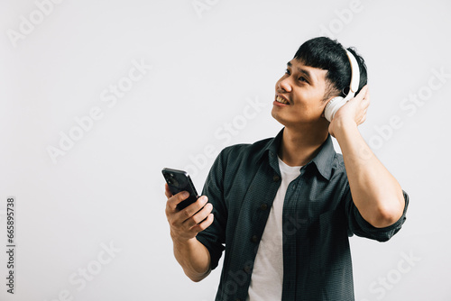 An excited man enjoys karaoke on his smartphone, singing with Bluetooth headphones. Studio shot isolated on white background, capturing his positive and musical spirit.