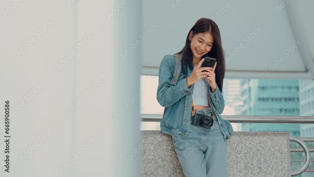 Young asian woman smiling, using mobile smart phone outdoor. Happy beautiful female wearing jeans jacket and holding smartphone at public city. Online technology and communication concept Young asian woman smiling, using mobile smart phone outdoor. Happy beautiful female wearing jeans jacket and holding smartphone at public city. Online technology and communication concept
