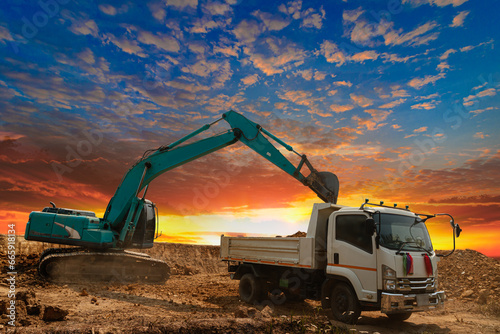 Crawler Excavator digging the soil into a truck  In the construction site on the sunset sky background .
